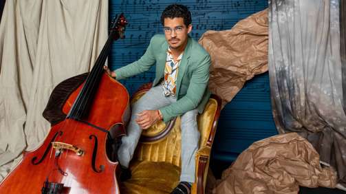 Marlon Martinez stands on a chair holding his cello.