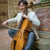 Antonio Lysy plays the cello while sitting on steps.