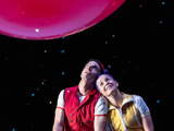 Photo of Seth Bloom and Christina Gelsone leaning their heads together, looking up at a large red balloon.