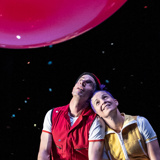 Photo of Seth Bloom and Christina Gelsone leaning their heads together, looking up at a large red balloon.