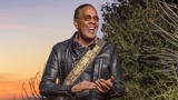 Stanley Clarke poses smiling before a sunset.