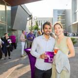 Image of a couple holding the BroadStage brochure in front of a table with purple tablecloth on the BroadStage plaza.