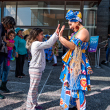Image of a dancer in costume high-fiving a young child on the BroadStage plaza.